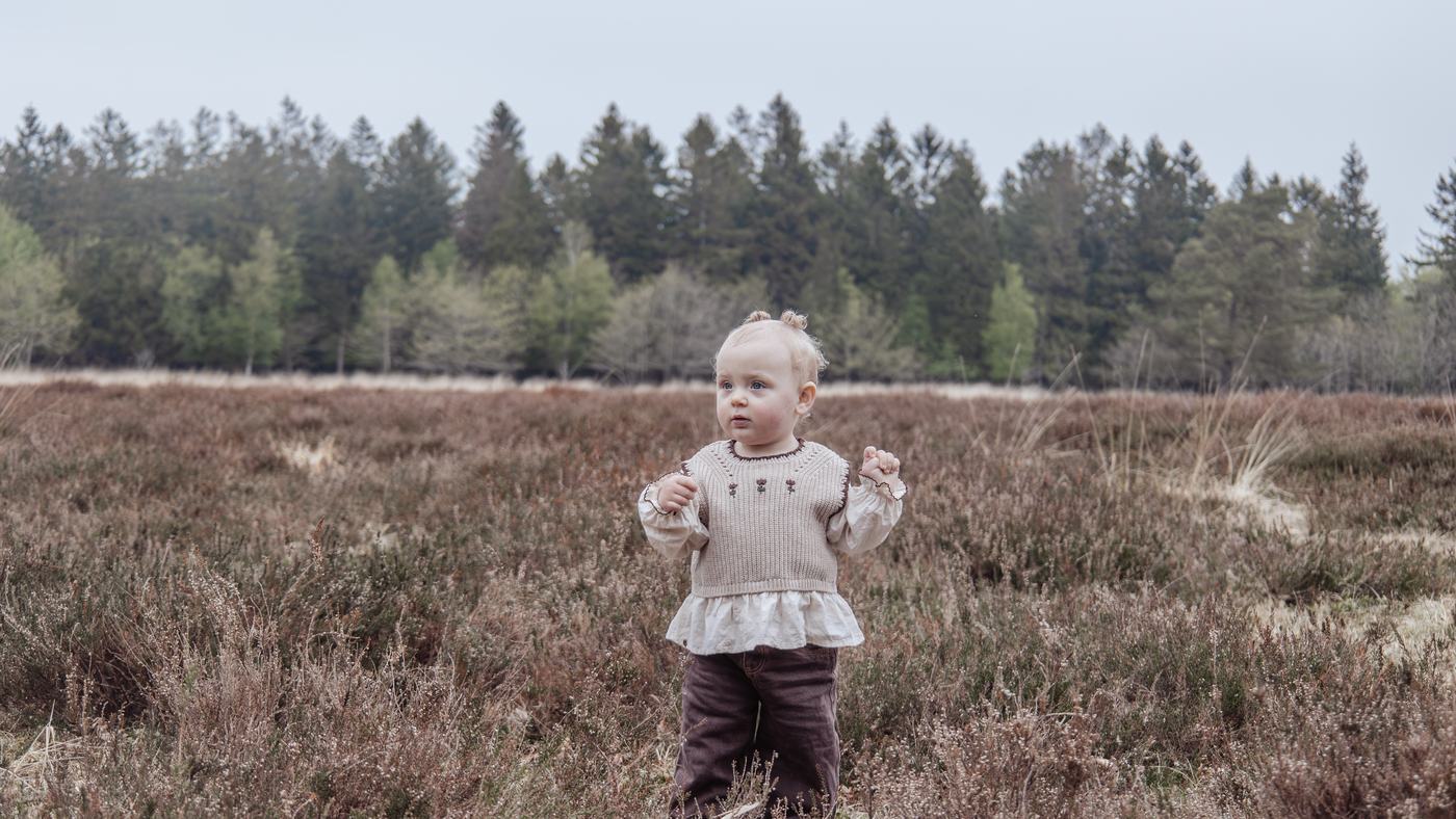 Lille barn står alene i den blomstrende lyng med skovbryn i baggrunden